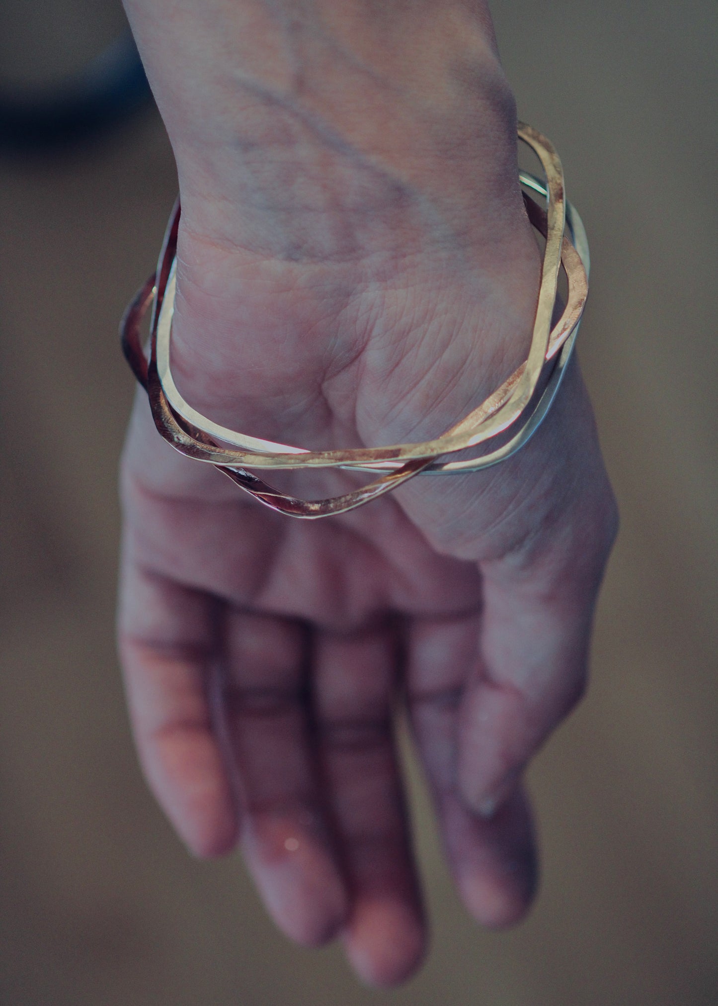 Hand wearing a square bangle stack in gold and silver against soft neutral background