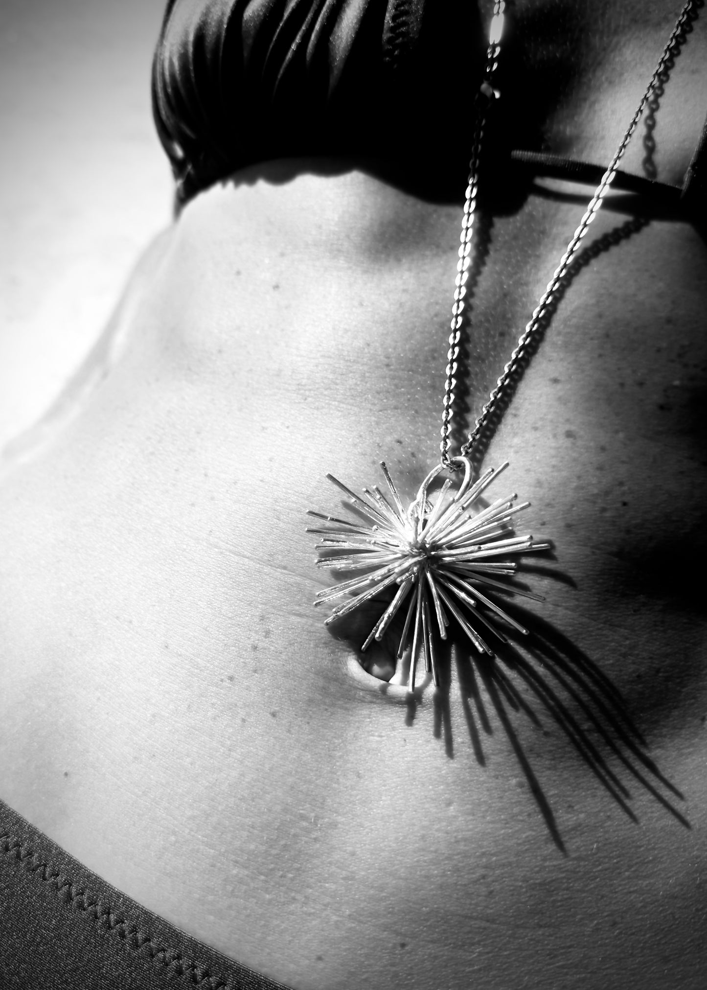 Black and white close-up of Beam necklace by Ninimosi, sculptural silver pendant casting shadows on body