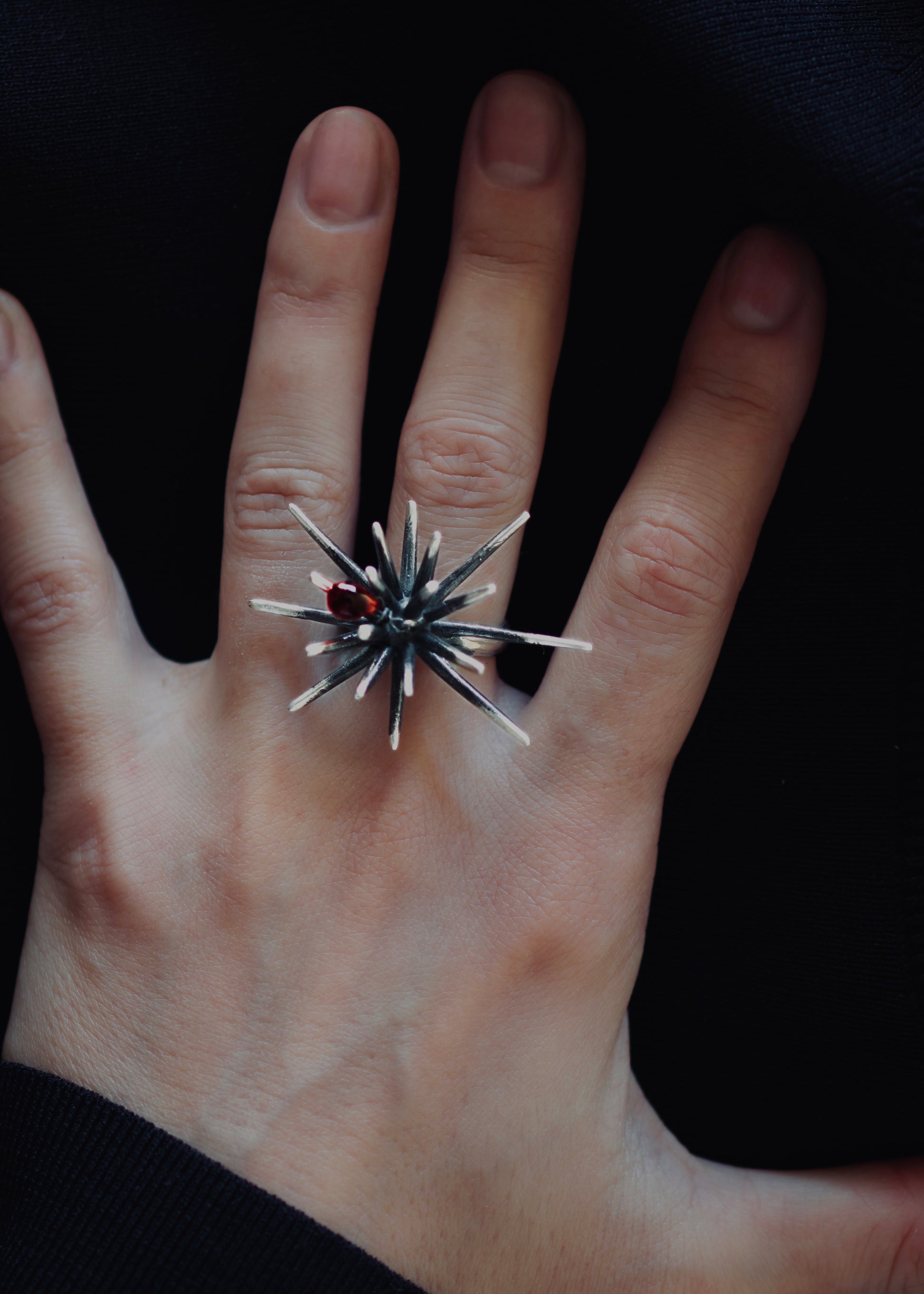 Side angle of adjustable sterling silver ring with spiked structure and red crystal detail, showing open band and patina texture