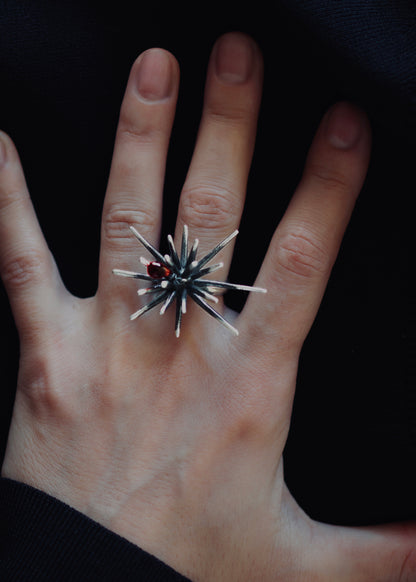 Side angle of adjustable sterling silver ring with spiked structure and red crystal detail, showing open band and patina texture