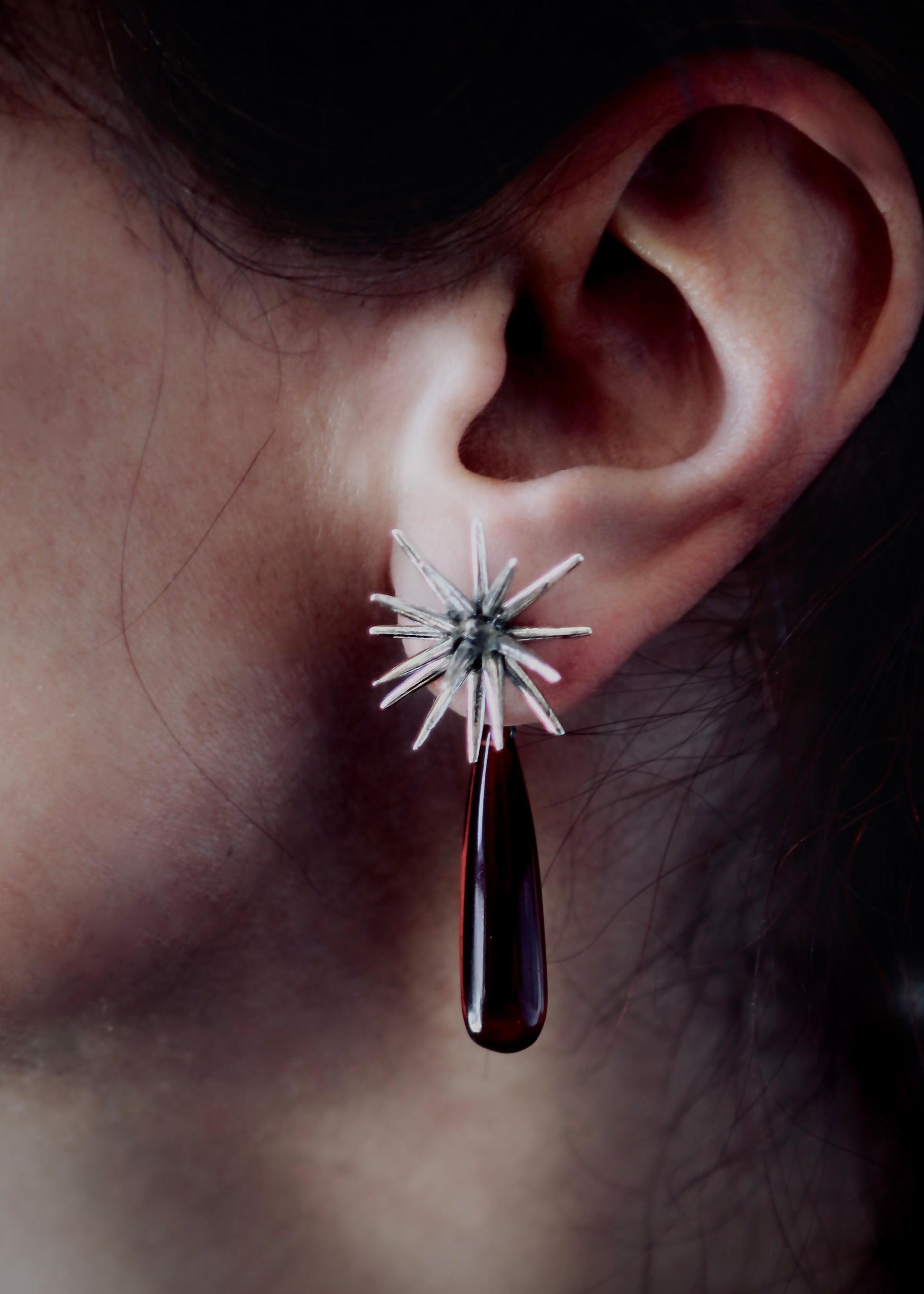 Silver Beam stud earring with ruby quartz teardrop pendant worn on ear, sculptural spike design with deep red drop