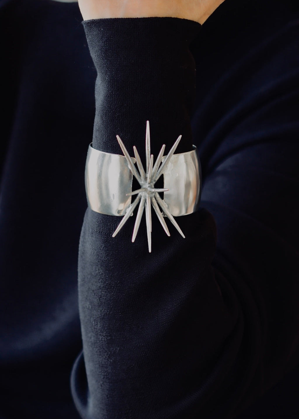 Sterling silver statement sculptural cuff on the wrist agains dark clothing background
