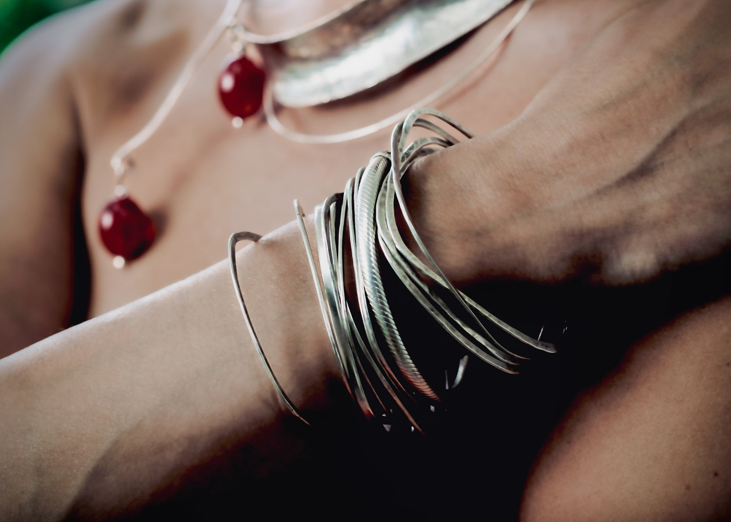 Close-up of stacked sterling silver bangles on wrist with red glass jewelry detail