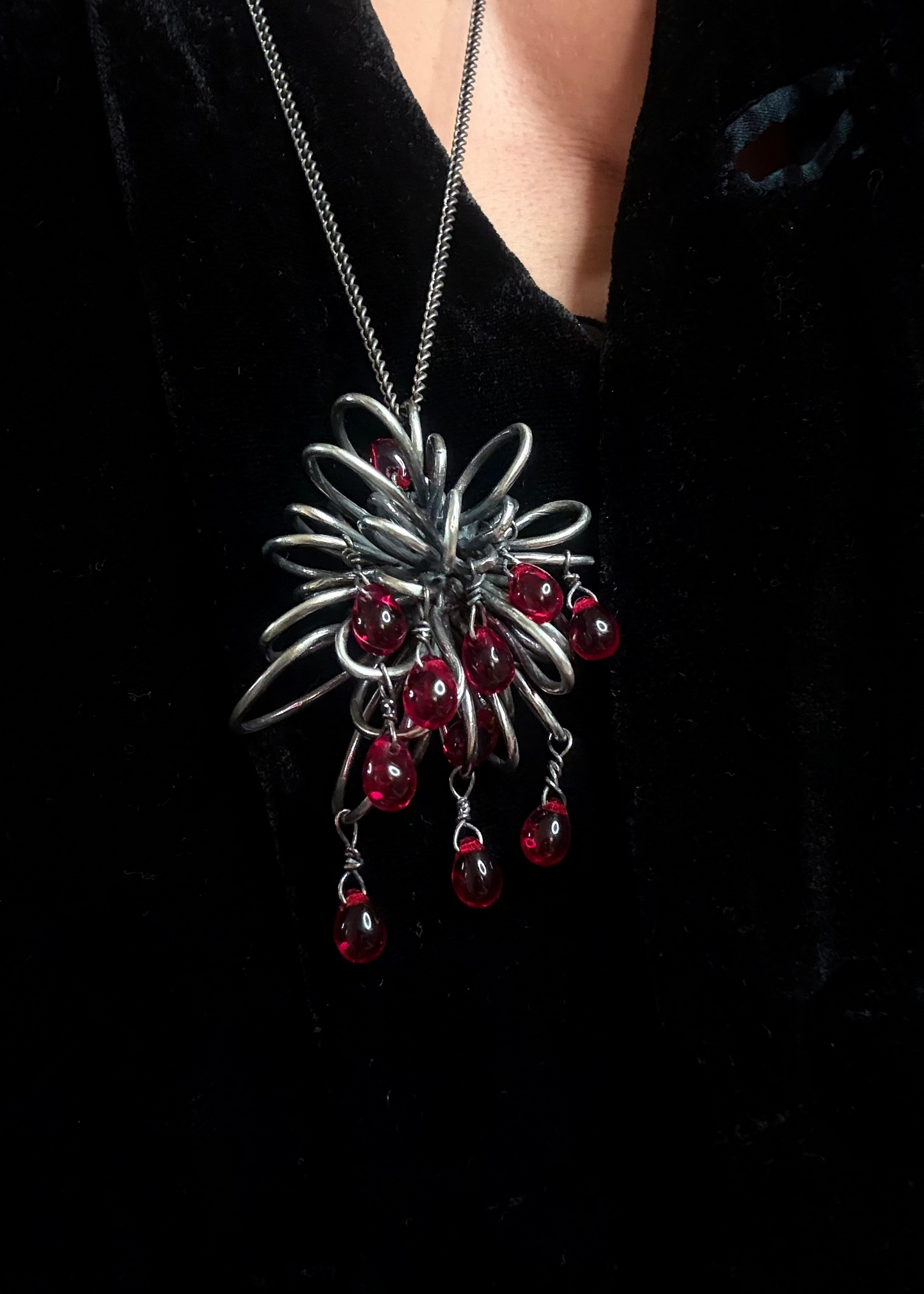 Close-up of Inversion necklace showing dense silver structure and multiple moving red Czech glass drops on chest