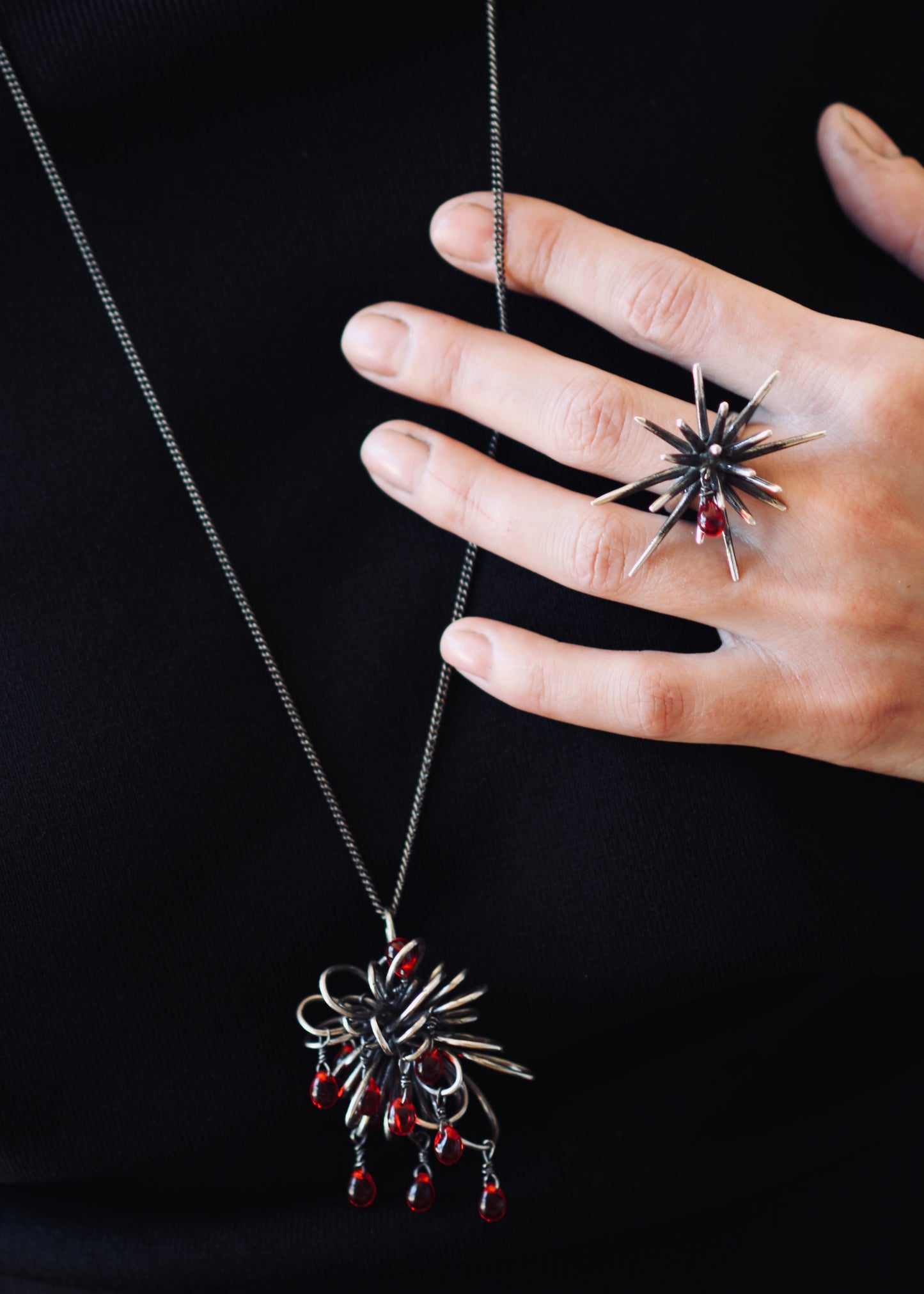 Model wearing sterling silver Inversion necklace with clustered sculptural pendant and dangling red glass drops against black jacket