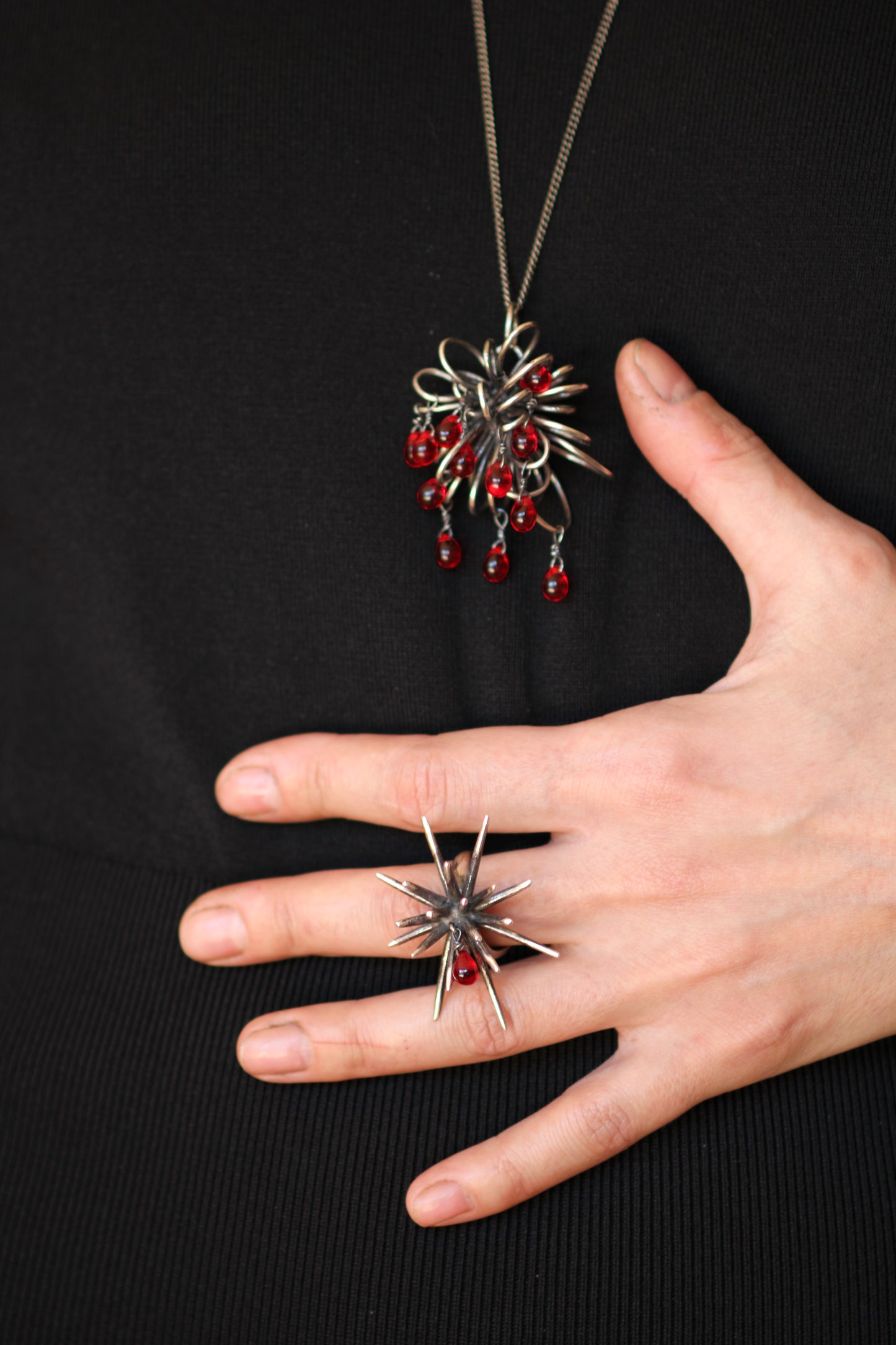 Sterling silver Inversion necklace with red glass drops worn with matching Beam ring on hand against dark background
