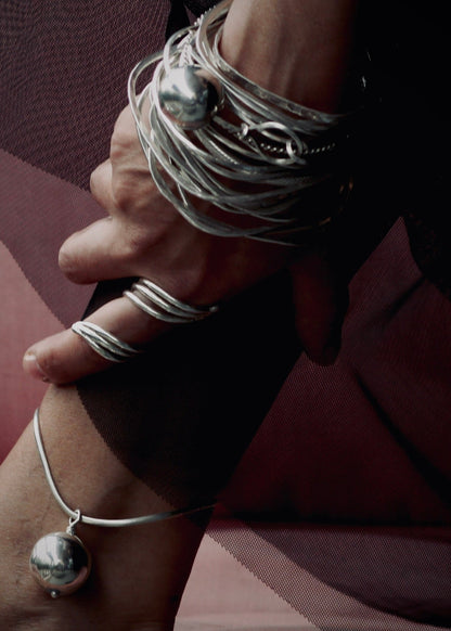 hand wearing silver stacked set of handcrafted bangles with sculptural ring and handcrafted sphere anklet