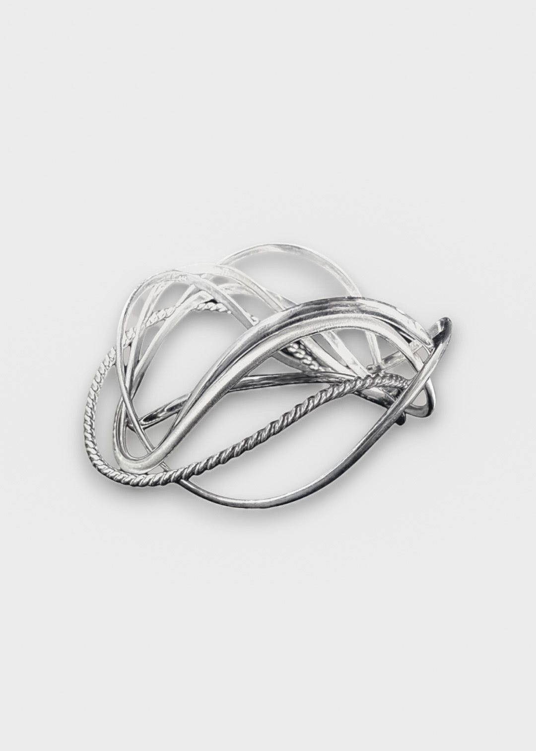 handcrafted silver wave bangle stack on neutral background, sculptural stackable jewelry