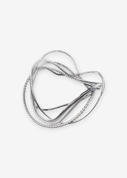 handcrafted silver wave bangle stack on neutral background, sculptural stackable jewelry in precious metal